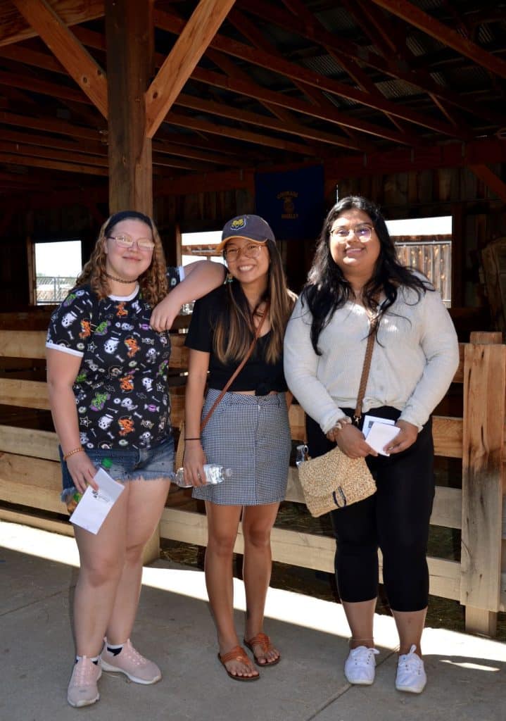 three friends stand arm-in-arm by the outdoor animal stables at the Centennial Village Museum during Potato Day