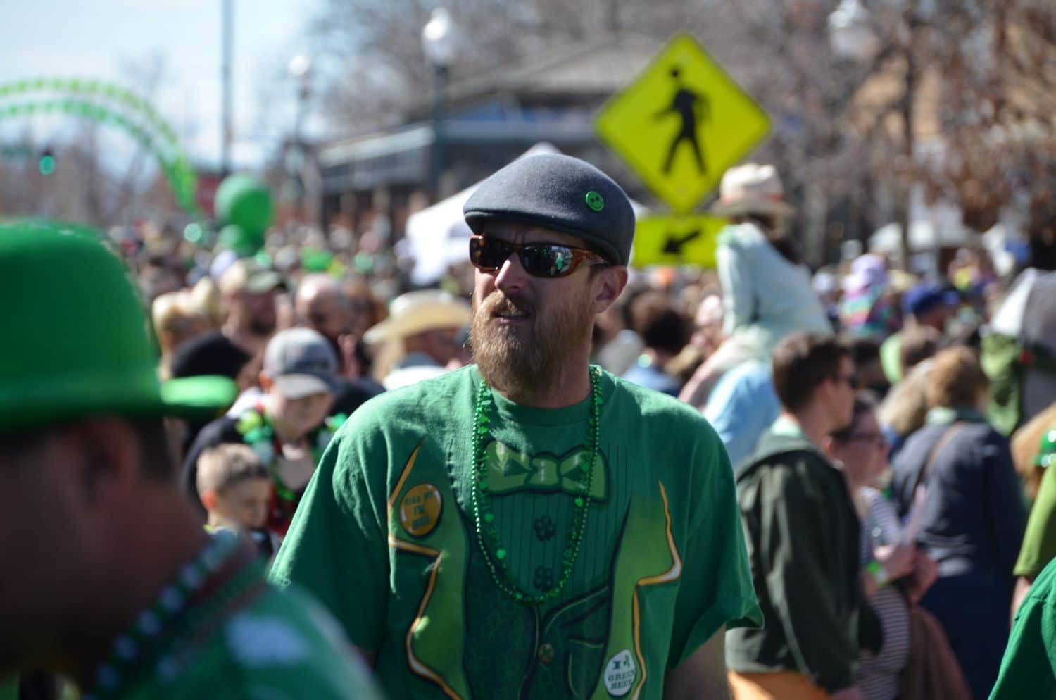 A red-haired man in sunglasses and a bright green t-shirts stands in a packed crowd in downtown Greeley, Colorado