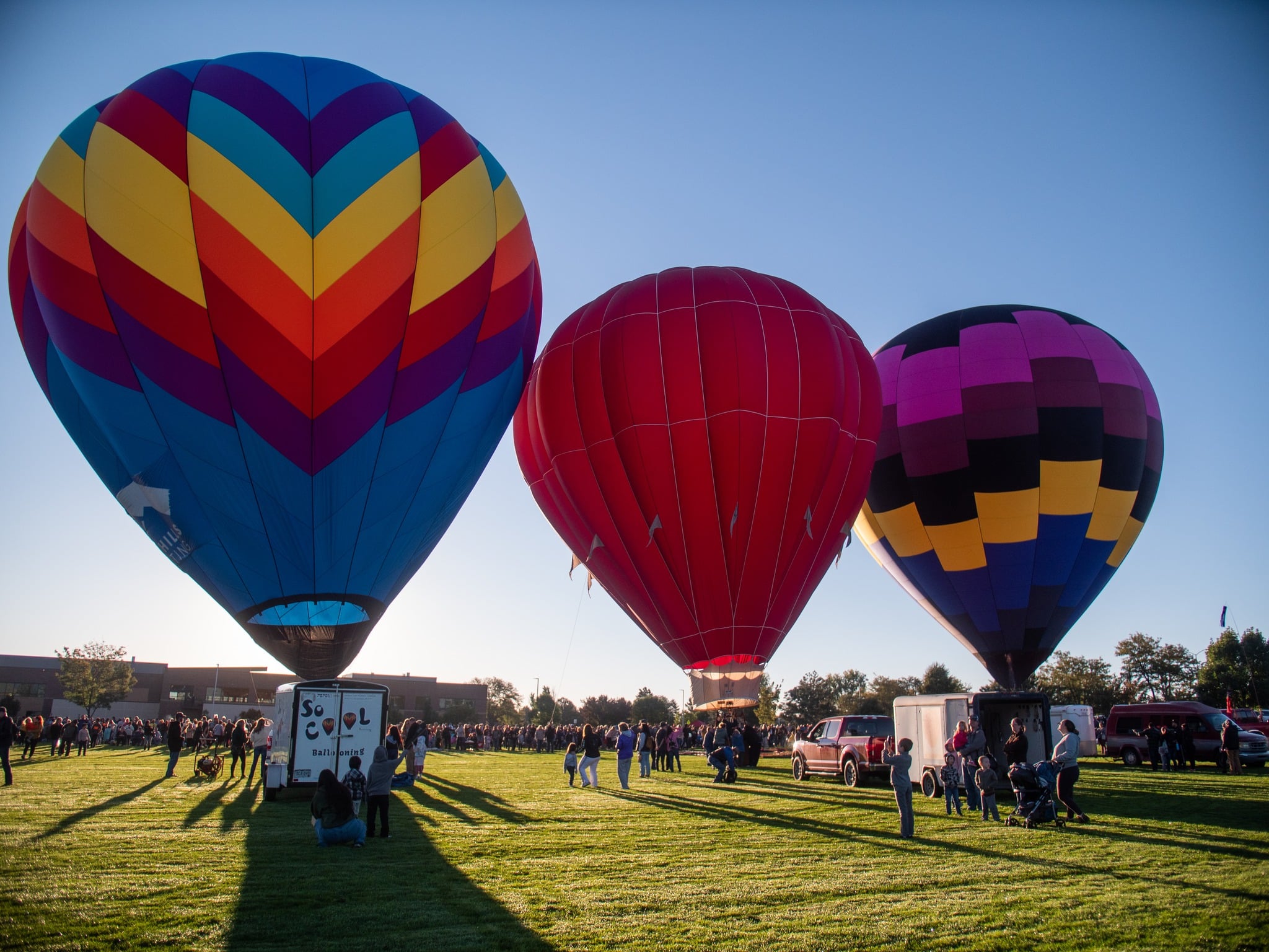 Three brightly colored hot air balloons sit poised for take off on a bright green lawn at Aims Community College in Greeley, Colorado