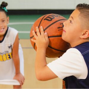 A young boy aims a basketball and prepares to shoot while two friends look on.
